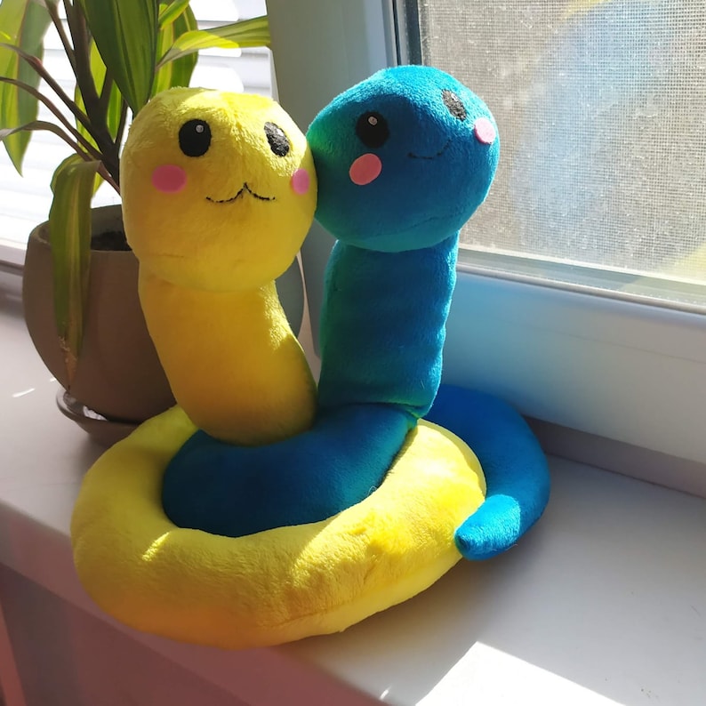 Pu&ograve; includere: Un giocattolo di peluche a forma di serpente giallo e blu con un viso sorridente. Il serpente &egrave; arrotolato in un cerchio.