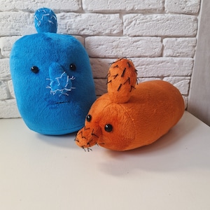 May include: Two plush toys shaped like cacti. One is blue with a stitched-on face and the other is orange with black stitching.