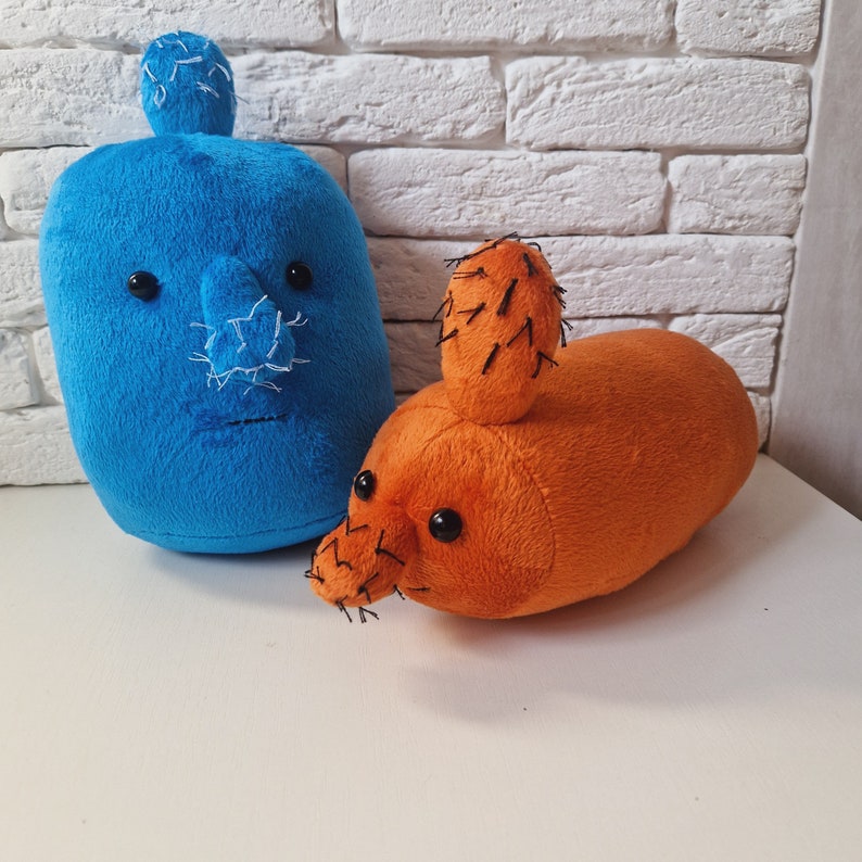May include: Two plush toys shaped like cacti. One is blue with a stitched-on face and the other is orange with black stitching.