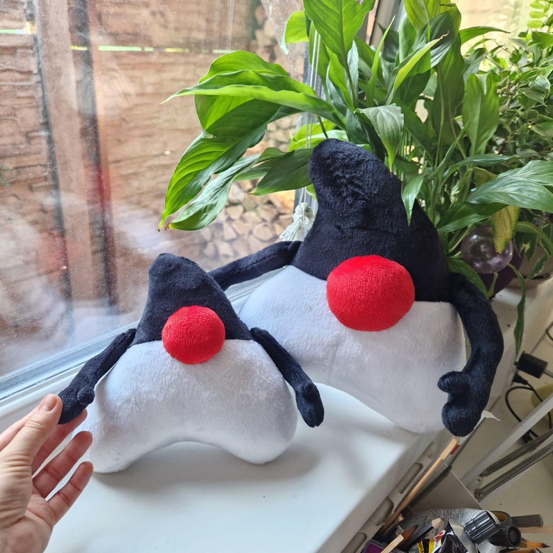 May include: Two plush toys shaped like the Linux Tux mascot. The larger toy is black and white with a red nose, while the smaller toy is black and white with a red nose. Both toys have black arms and legs.