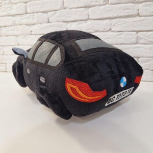 以下が含まれることがあります： 青と白のBMWロゴ、赤いテールライト、ナンバープレートに「BC 7223 TE」と書いてある黒いぬいぐるみ車。