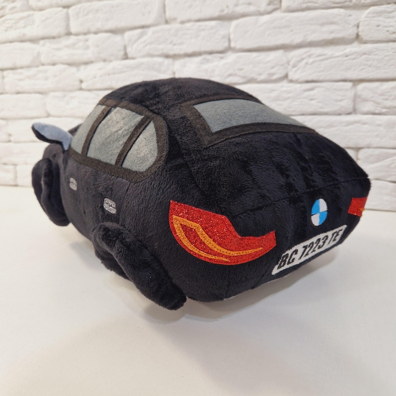 以下が含まれることがあります： 青と白のBMWロゴ、赤いテールライト、ナンバープレートに「BC 7223 TE」と書いてある黒いぬいぐるみ車。