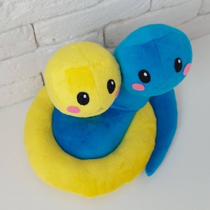 Pu&ograve; includere: Un giocattolo di peluche a forma di serpente giallo e blu con un viso carino. Il serpente &egrave; arrotolato in un cerchio con la testa appoggiata sulla coda.