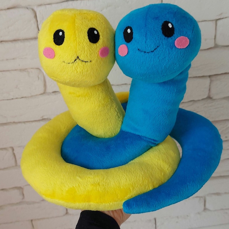 Pu&ograve; includere: Un serpente di peluche giallo e blu con un viso sorridente. Il serpente &egrave; arrotolato in un cerchio.