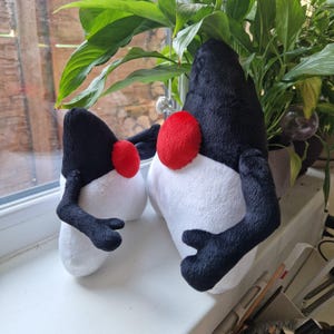 May include: Two plush toys shaped like the Linux mascot, Tux. The larger Tux is black and white with a red nose, while the smaller Tux is black and white with a red nose. Both Tuxes have black arms and legs.