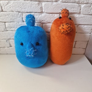 May include: Two plush toys shaped like potatoes. One is blue with a stitched-on face and the other is orange with a green cactus on top.
