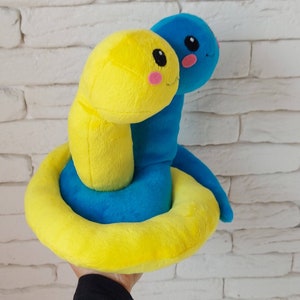Pu&ograve; includere: Un giocattolo di peluche a forma di serpente giallo e blu con un viso sorridente. Il serpente &egrave; arrotolato in un cerchio, con la coda infilata sotto la testa.