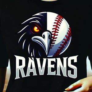 Op de afbeelding: Een zwart T-shirt met een afbeelding van een raaf met een honkbal als hoofd. De tekst "RAVENS" is onder de afbeelding gedrukt.