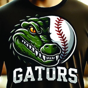 May include: A digital download of a graphic design featuring a green alligator with a baseball stitched with red seams. The alligator's mouth is open and its teeth are visible. The text "GATORS" is below the alligator. The design is on a black t-shirt.