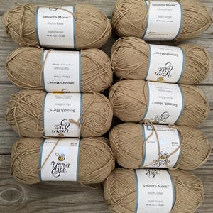 May include: A collection of light taupe yarn skeins. Each skein is labeled "Smooth Move Micro Fiber" and "Yarn Bee". The yarn is a neutral color, suitable for various knitting or crochet projects. The image shows multiple skeins.