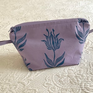 May include: A lavender zippered pouch with a floral design. The pouch has two handles and a zipper closure.