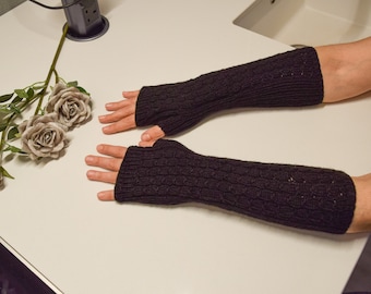 May include: A pair of black fingerless gloves with a cable knit pattern. The gloves are shown on a white surface.