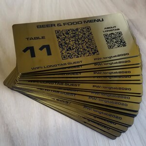 May include: A stack of gold-coloured table number signs with a black QR code and the text "BEER & FOOD MENU", "TABLE 11", "WIFI: LONGTAB GUEST", and "PW: longtab2020".
