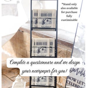 May include: A tall black metal display stand with three wire mesh shelves holding stacks of newspapers. The top sign reads The Newlywed Times PLEASE TAKE ONE. Each newspaper features a black and white photo and the text BREAKING NEWS!! RYAN & JENNIFER ARE GETTING MARRIED. The stand has a slim, vertical frame design.
