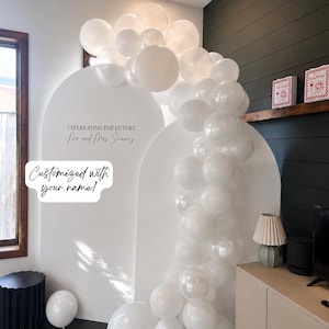 Può includere: Uno sfondo ad arco bianco con il testo CELEBRATING THE FUTURE Mr and Mrs Suarez e una ghirlanda di palloncini bianchi drappeggiata sulla parte superiore e laterale. È incluso un fumetto bianco con il testo Customized with your name.