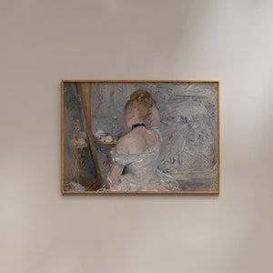May include: A painting of a woman in a white dress, sitting in front of a mirror, with her hair up. The painting is in a gold frame and is hanging on a white wall.