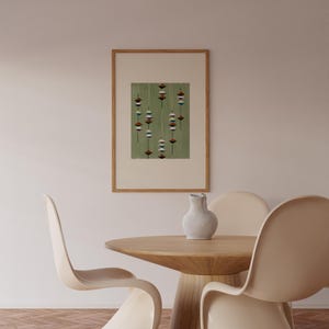 May include: A framed artwork featuring a green background with a pattern of hanging, stylized shapes in shades of red, white, and blue. The artwork is displayed above a wooden table and chairs in a neutral-toned room.