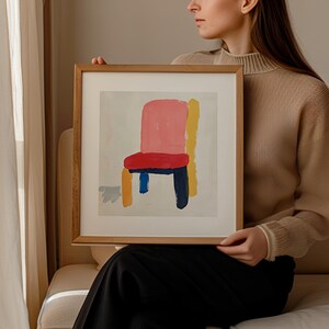 May include: A framed abstract painting of a chair with a pink seat, red cushion, yellow and blue legs, and a white background.