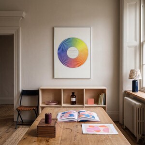 Framed color theory wall art displayed above a wooden desk in a warm creative workspace, featuring a vintage chromatic wheel with rainbow hues on an ivory ground. Colorful office wall decor for an artist studio, designer workspace, craft room, home office or creative interior with vintage scientific poster character.