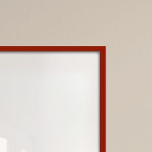May include: A corner view of a white picture frame with a dark red border. The frame is set against a light beige background. The frame's clean lines and bold color contrast create a simple, modern aesthetic.