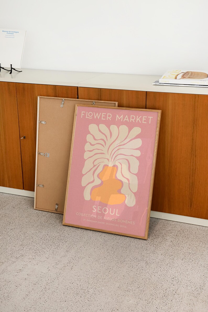 May include: A framed poster with a pink background and a white and orange abstract floral design. The poster reads "FLOWER MARKET SEOUL COLLECTION DE FLEURS BOHEMES 37. GANGNAM-DATRE SEOCHO-GU SEOUL".