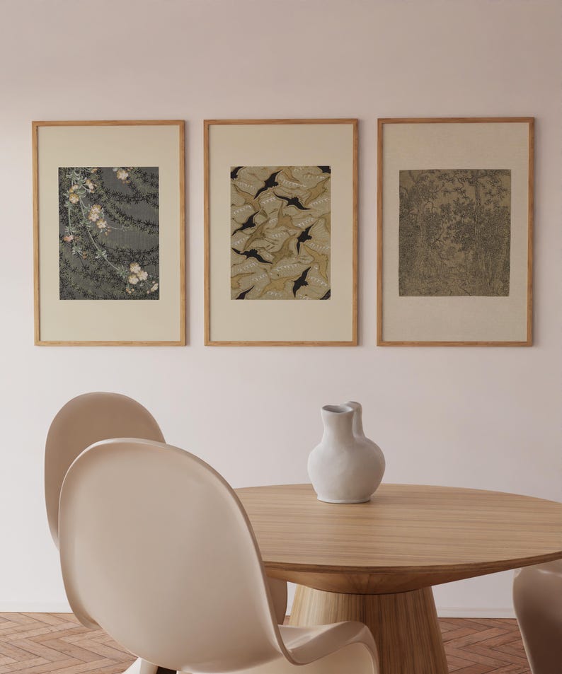 Gallery wall set of three framed Japanese art prints featuring flowering branches, decorative leaf patterns, and a woodland landscape, displayed above a round oak dining table in a warm dining room.