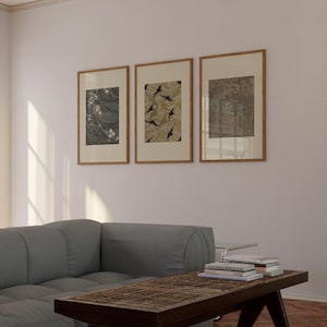 Set of three framed vintage botanical wall art prints featuring floral textile, leaf pattern, and forest drawings, displayed above a gray sofa in a neutral living room. Earthy gallery wall decor for Japandi and organic modern interiors.