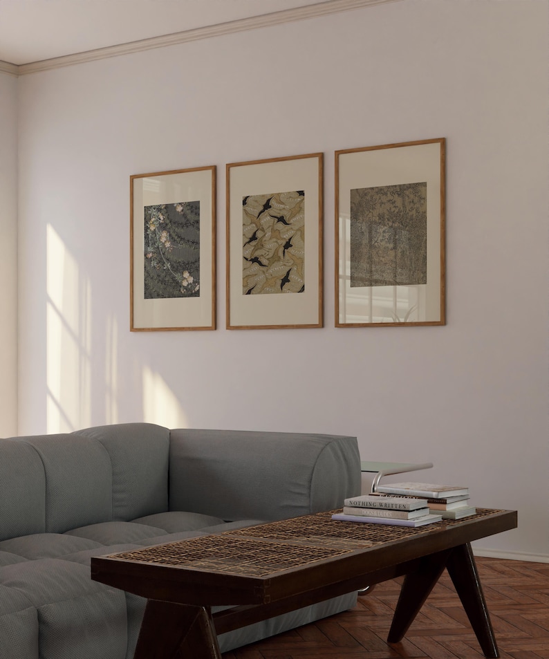 Set of three framed vintage botanical wall art prints featuring floral textile, leaf pattern, and forest drawings, displayed above a gray sofa in a neutral living room. Earthy gallery wall decor for Japandi and organic modern interiors.