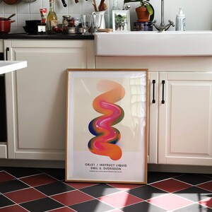 May include: A framed abstract art print with a colorful, swirling design in shades of pink, orange, and blue. The print is titled "OBJ21 / INSTRUCT LIQUID EMIL U. SVERISSON" and is displayed on a white wall in a kitchen.