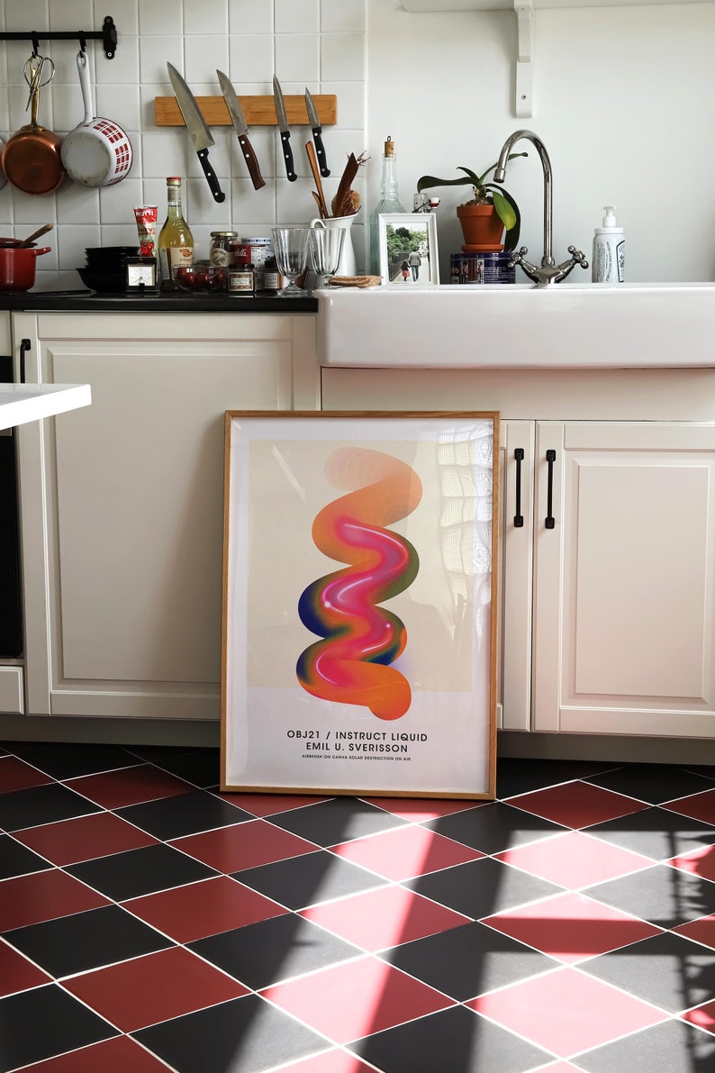 May include: A framed abstract art print with a colorful, swirling design in shades of pink, orange, and blue. The print is titled "OBJ21 / INSTRUCT LIQUID EMIL U. SVERISSON" and is displayed on a white wall in a kitchen.