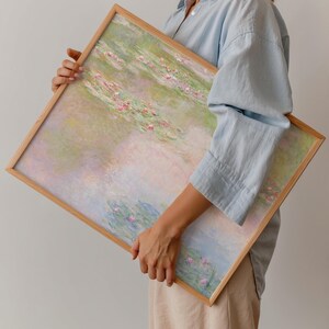 Large Claude Monet Water Lilies print held in a natural oak frame, showing soft pink water lilies with pastel green, blue and lavender reflections. Framed impressionist landscape art with a dreamy palette for bedroom, living room and serene modern interiors.