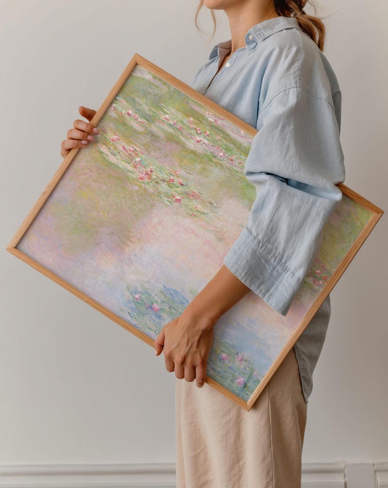 Large Claude Monet Water Lilies print held in a natural oak frame, showing soft pink water lilies with pastel green, blue and lavender reflections. Framed impressionist landscape art with a dreamy palette for bedroom, living room and serene modern interiors.