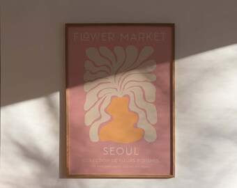 Puede incluir: Una impresión enmarcada con un fondo rosa y una ilustración estilizada de una flor en crema y naranja. El texto "FLOWER MARKET" está en la parte superior de la impresión, y el texto "SEOUL COLLECTION DE FLEURS BOHEMES 27, GANGNAM-DAERO SEOCHO-GU, SEOUL" está en la parte inferior.