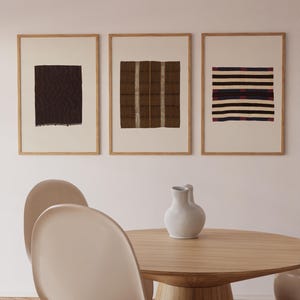 Puede incluir: Tres impresiones art&iacute;sticas abstractas enmarcadas. Las impresiones presentan patrones texturizados en tonos marrones, negros y azules, sobre un fondo crema. Los marcos son de madera clara. Una mesa redonda de madera y sillas est&aacute;n en primer plano.