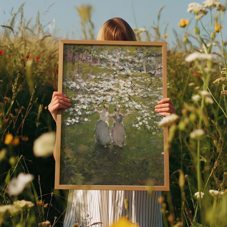 Op de afbeelding: Een ingelijst schilderij van twee vrouwen in witte jurken die onder een bloeiende boom staan. Het schilderij is tegen een groene achtergrond met witte bloemen.