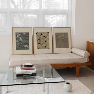 Set of three framed vintage wall art prints featuring floral textile, botanical leaf, and detailed forest designs, styled together in a bright neutral living room. Earthy gallery wall set for Japandi, organic modern, and eclectic interiors.