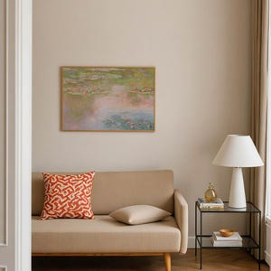 Pastel Monet Water Lilies wall art displayed above a beige sofa in a warm modern living room. Soft pink, sage green, lavender and blue tones create a dreamy impressionist landscape print for above sofa decor, bedroom or eclectic interiors.