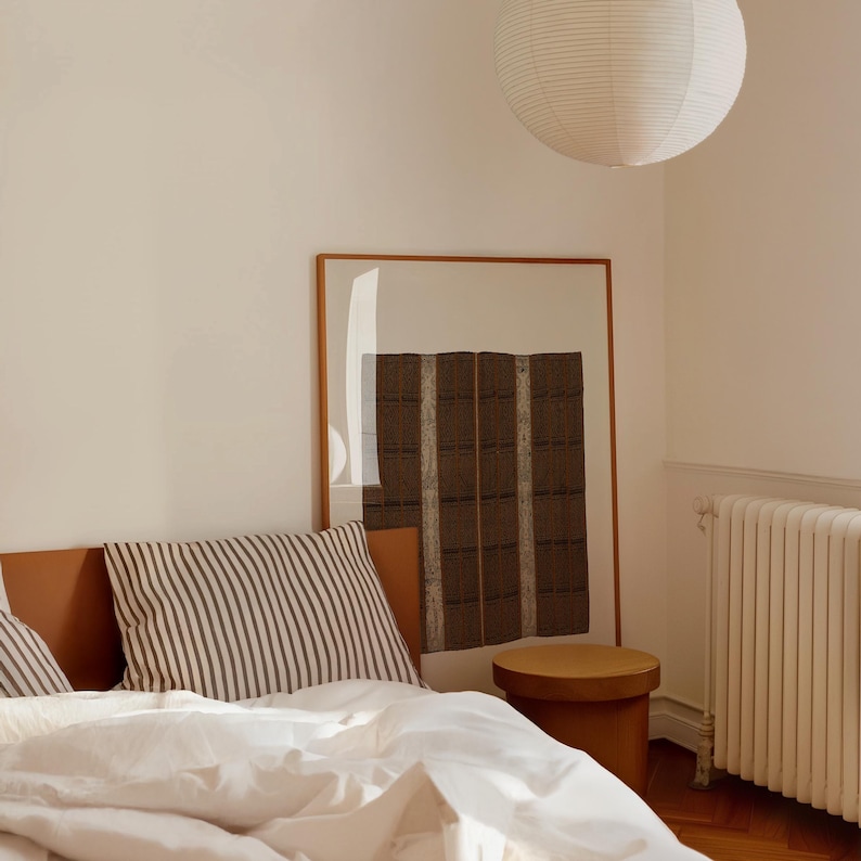 Brown vintage textile print in a natural oak frame beside a bed. Woven pattern wall art for bedroom decor, Japandi interiors, neutral homes, and organic modern spaces.