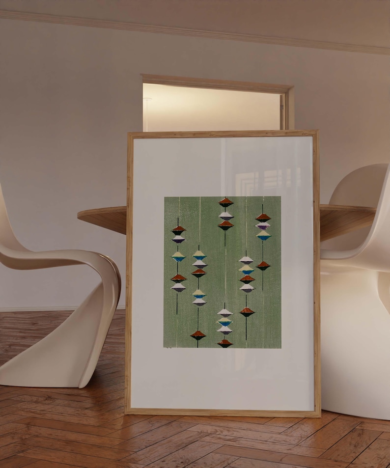 May include: A framed abstract print featuring a green background with vertical lines and colorful, geometric shapes. The artwork is displayed in a light wood frame, leaning against a wall. The print's design includes red, white, blue, and brown elements.