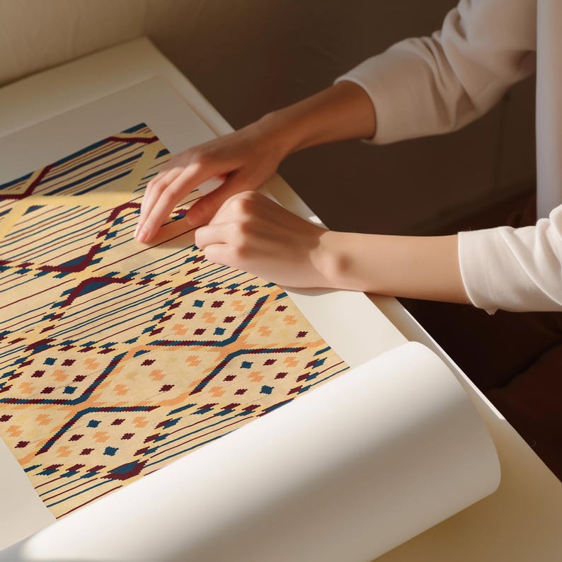 K&ouml;nnte beinhalten: Nahaufnahme eines gemusterten Textils mit beigem Hintergrund und geometrischen Designs in Marineblau, Burgunderrot und Pfirsich. Das Textil wird auf einer wei&szlig;en Oberfl&auml;che bearbeitet. Das Design zeigt Linien, Rauten und andere Formen.