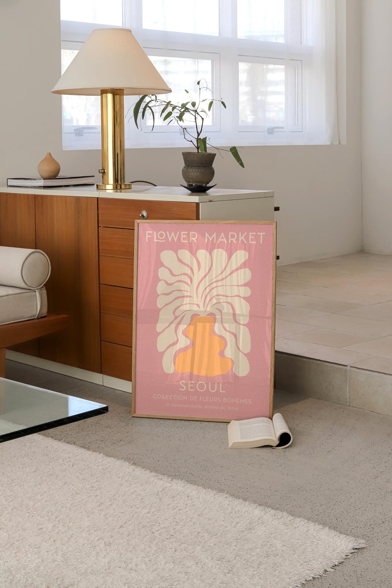 May include: A pink poster with a white and orange abstract floral design. The poster has the text "FLOWER MARKET" and "SEOUL" in white. The text below "SEOUL" reads "COLLECTION DE FLEURS BOHEMES" and "27, BOULEVARD SEOUL, 00000 SEOUL".