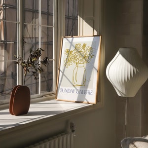 May include: A framed print of a line drawing of a bouquet of flowers in a vase. The print is on a white background with the text "SUNDAY GALERIE" in blue at the bottom.