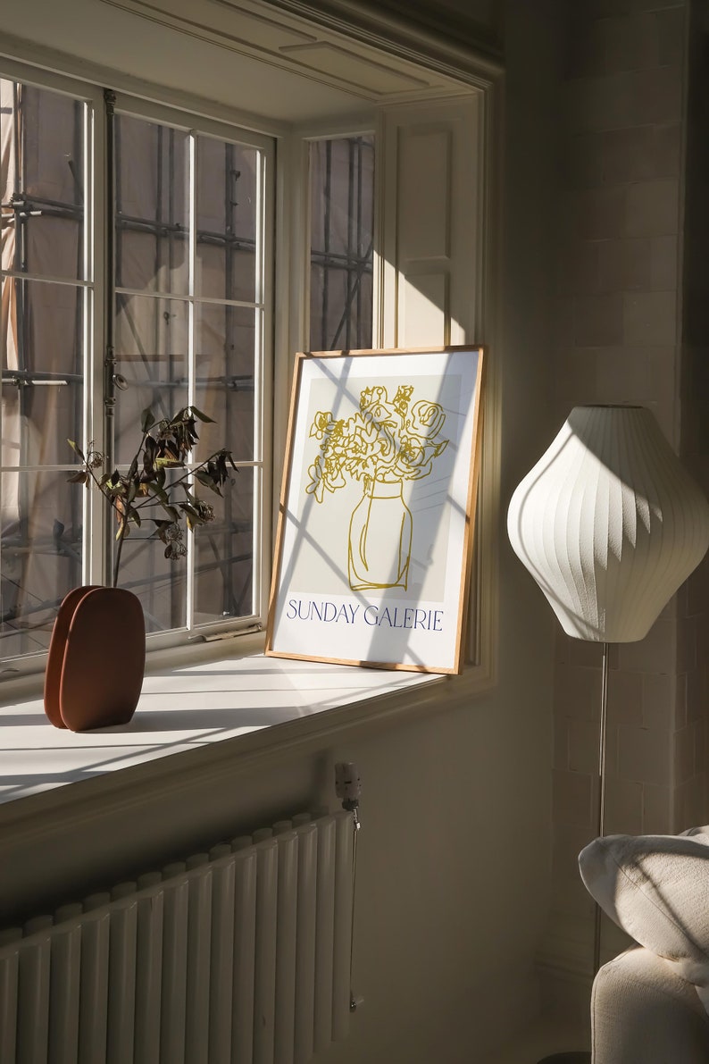 May include: A framed print of a line drawing of a bouquet of flowers in a vase. The print is on a white background with the text "SUNDAY GALERIE" in blue at the bottom.