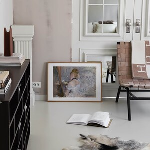 May include: A framed painting of a woman in a white dress sitting on a chair. The painting is hanging on a light pink wall in a room with a white rug and a wooden chair.