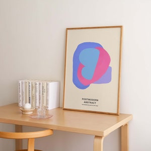 Peut inclure: Une impression encadr&eacute;e avec un motif abstrait bleu clair, rose et violet. L'impression est intitul&eacute;e "Postmodern Abstract" et provient de "The Modern Gallery of Art 2020". L'impression est sur un bureau en bois avec une pile de livres et un verre d'eau.