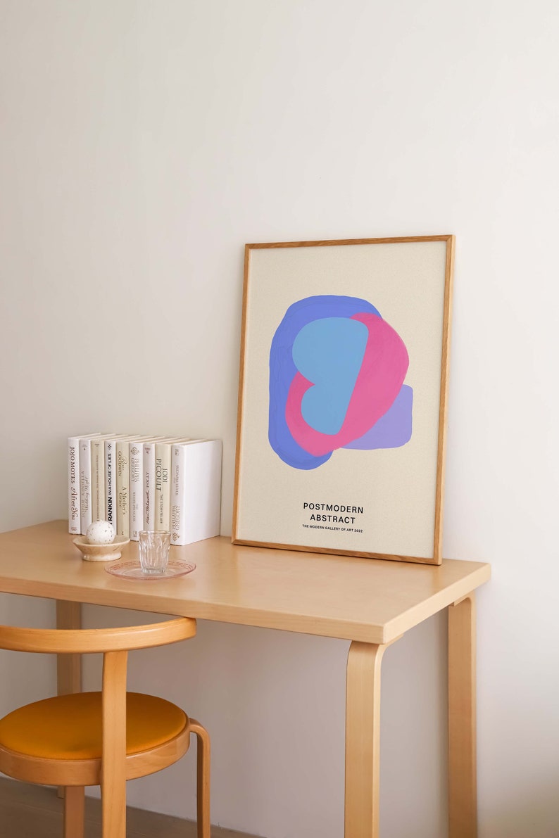 Peut inclure: Une impression encadr&eacute;e avec un motif abstrait bleu clair, rose et violet. L'impression est intitul&eacute;e "Postmodern Abstract" et provient de "The Modern Gallery of Art 2020". L'impression est sur un bureau en bois avec une pile de livres et un verre d'eau.