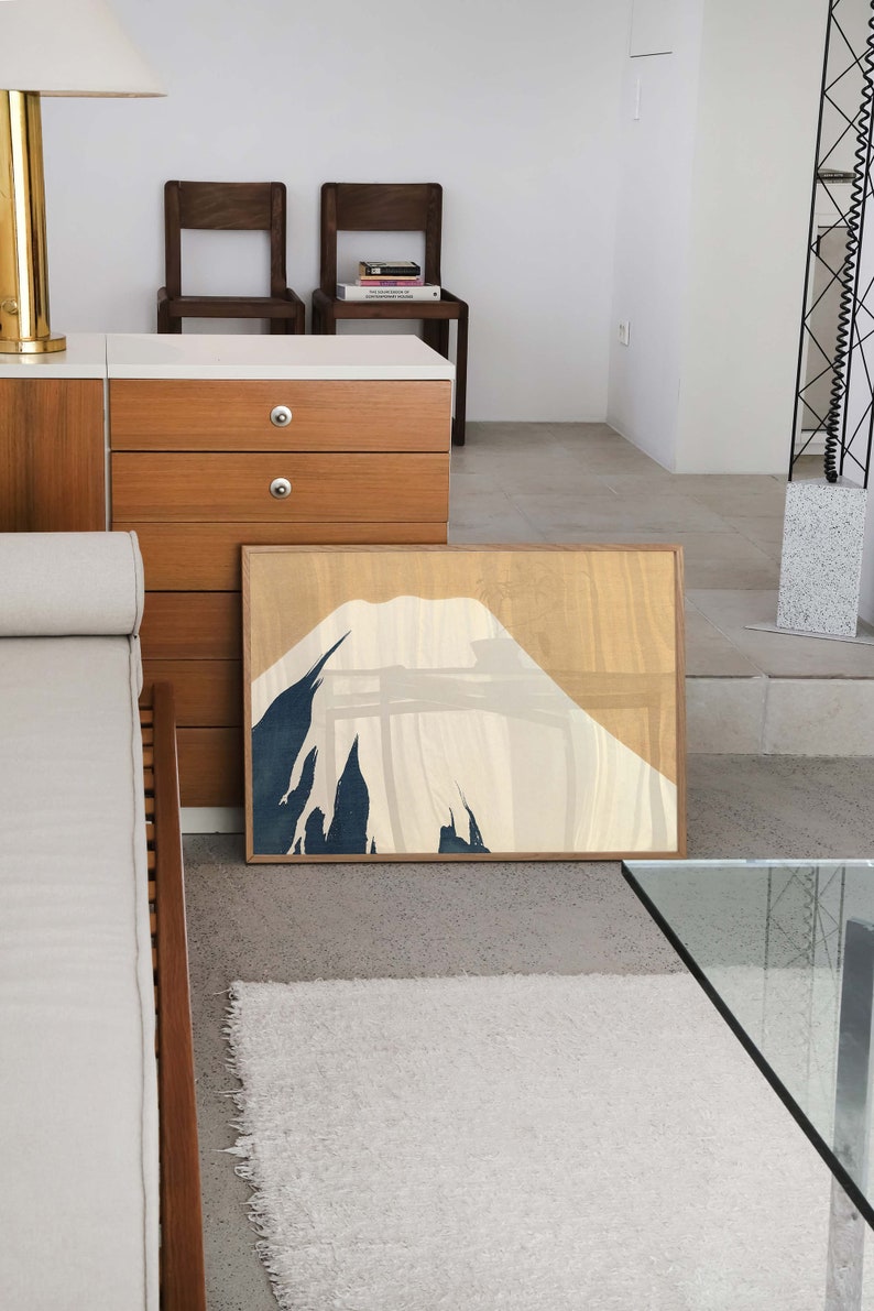 以下が含まれることがあります： 青、白、ベージュの色合いでスタイリッシュな山岳風景の額装されたプリント。山は、テクスチャのある背景でミニマルなスタイルで描かれています。