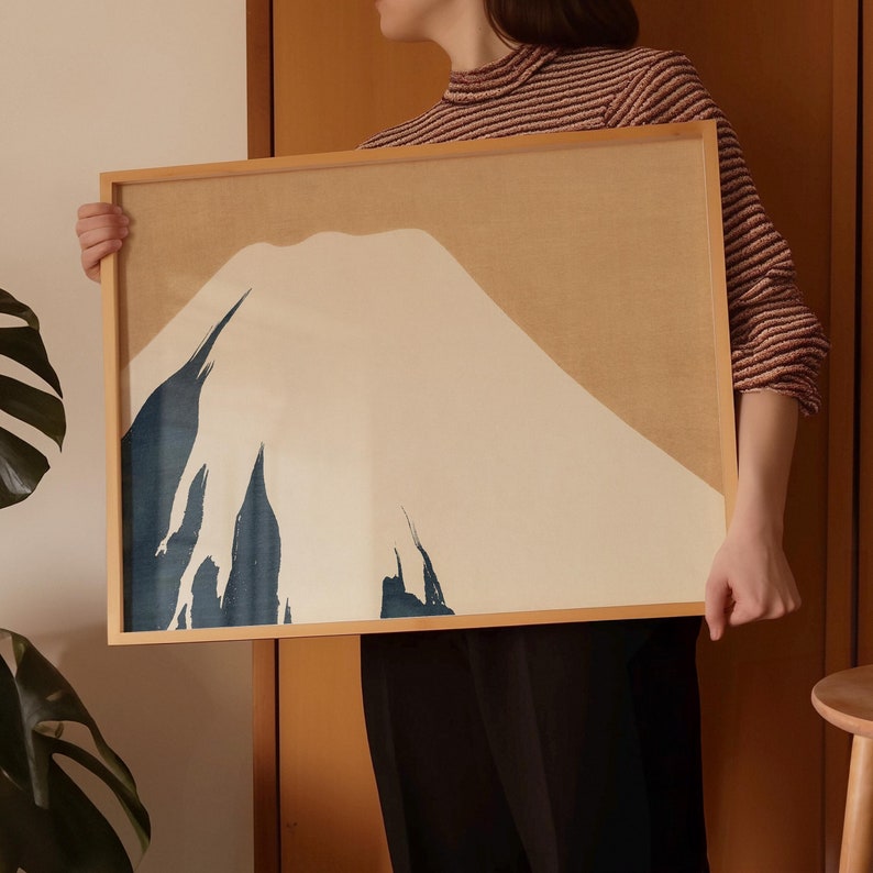 以下が含まれることがあります： 白、青、茶色の色合いでスタイリッシュな山岳風景が描かれた額装されたプリント。山は、青い筆致がいくつか加えられたミニマルなスタイルで描かれている。
