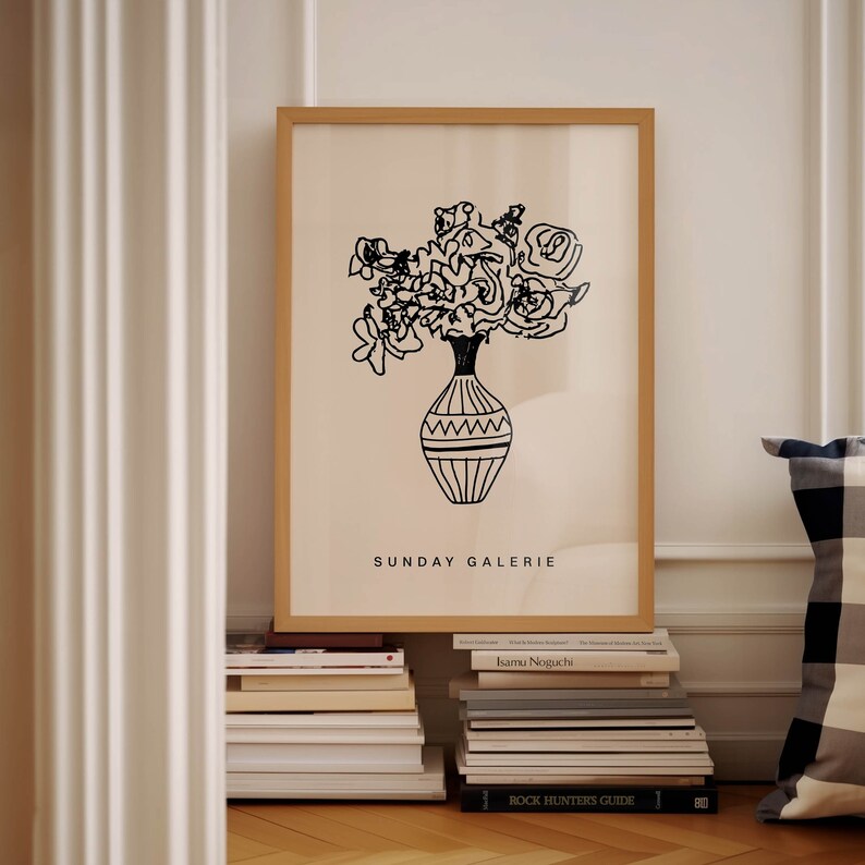 May include: A black and white line drawing of a bouquet of flowers in a vase. The vase has a geometric pattern. The image is framed in a light wood frame and has the text "SUNDAY GALERIE" at the bottom.