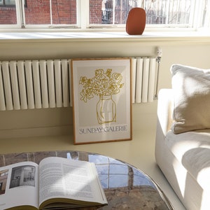 May include: A framed print with a gold line drawing of flowers in a vase. The print has the text "SUNDAY GALERIE" at the bottom.